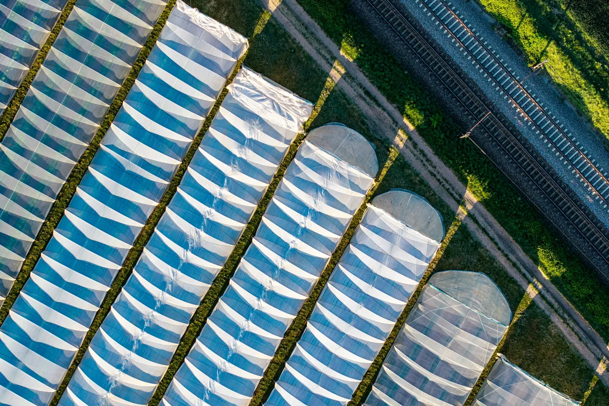Luchtfoto van kassen naast een spoorlijn en groene weilanden.