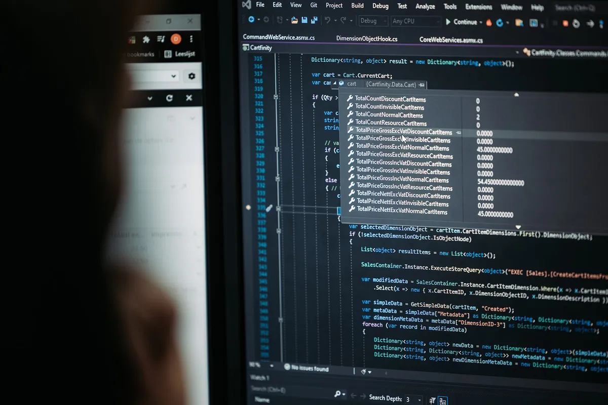 Program code on a screen at Infodatek Group, with a colleague in the foreground.