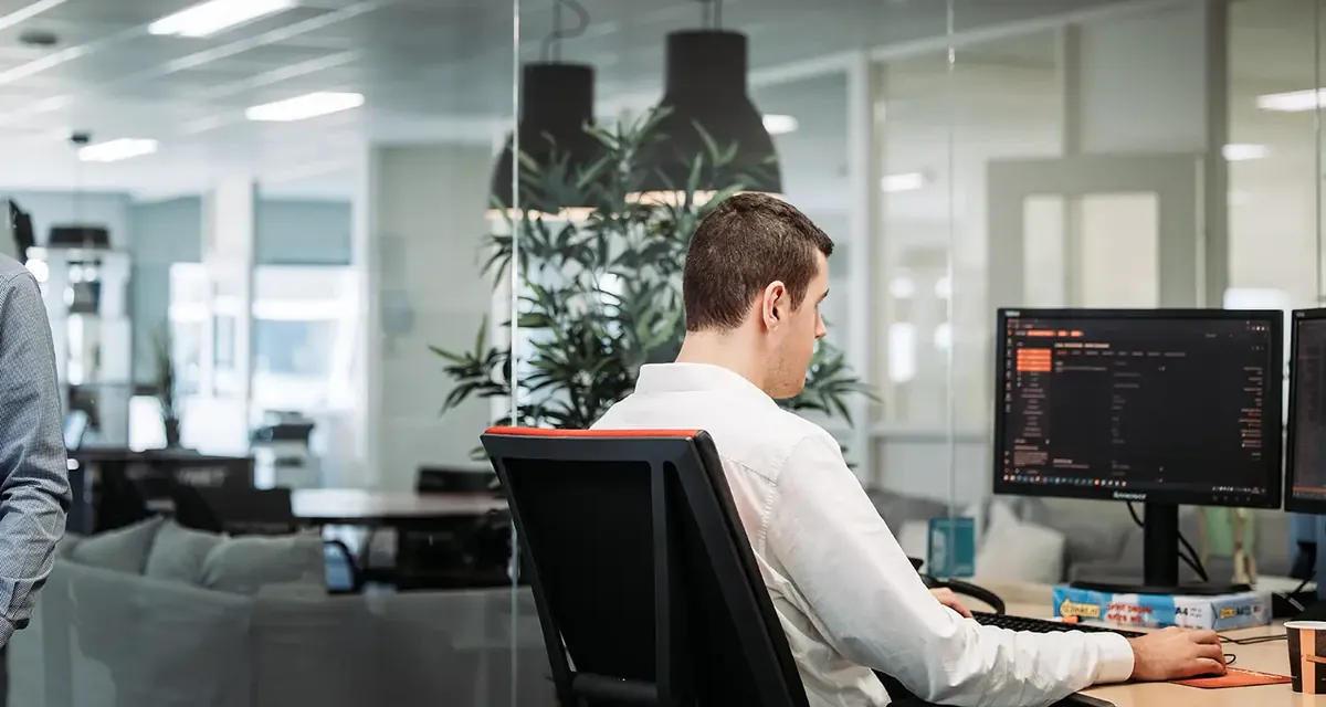 An Infodatek Group engineer behind his screen, with glass walls and plants in the background.