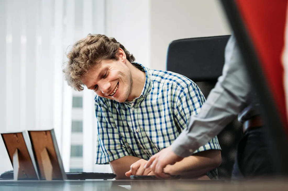 An Infodatek Group colleague laughing behind his laptop while a colleague beside him leans in and points something out.