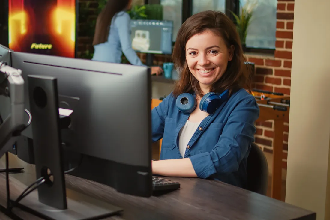 A smiling IT specialist at her computer, with headphones around her neck.