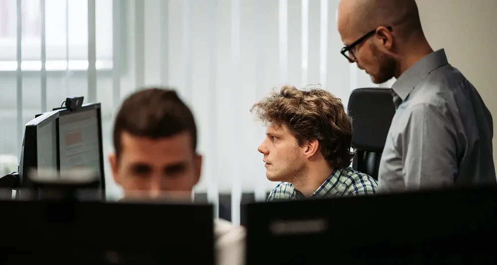 Drie collega's van Infodatek Group achter hun schermen op kantoor in Terneuzen, een van hen kijkt mee over de schouder.