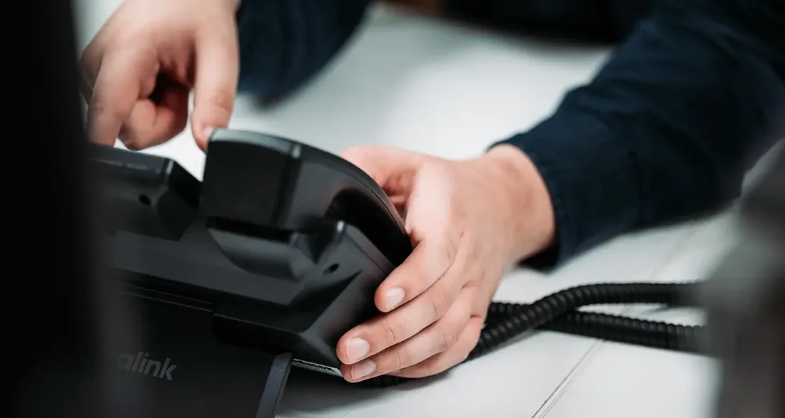 An Infodatek Group colleague picking up the handset of a desk phone.